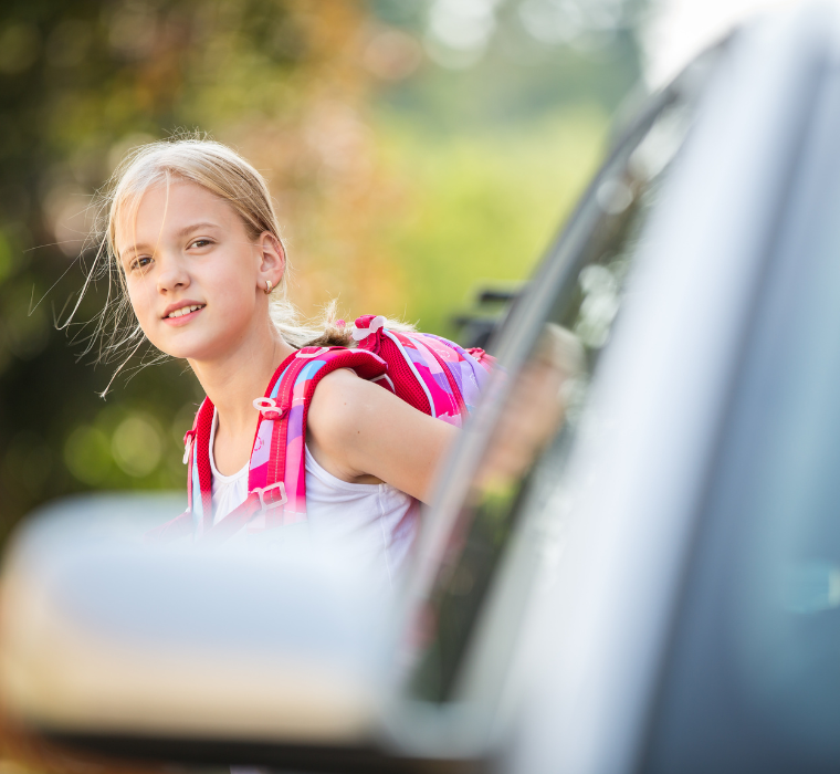 Une fillette regarde depuis derrière une voiture