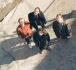 Les quatre musiciens se tiennent sur le trottoir et regardent le photographe.
